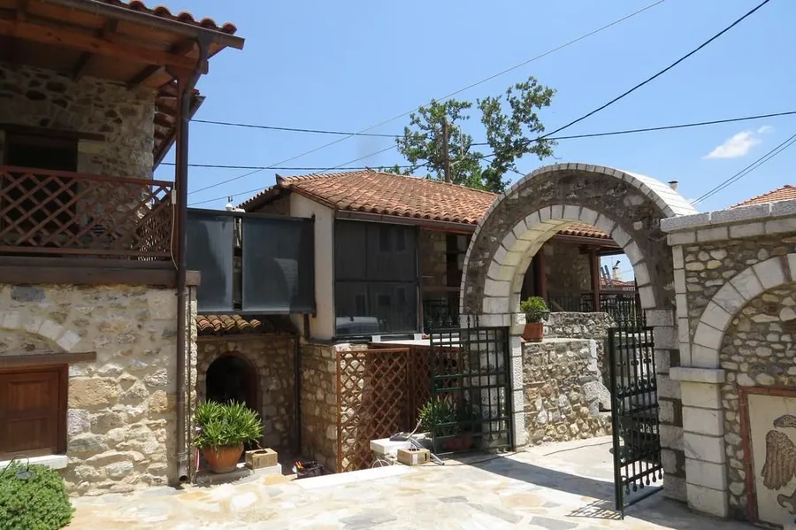 Πέτρινη καμάρα με σιδερένια αυλόπορτα και ξύλινο μπαλκόνι